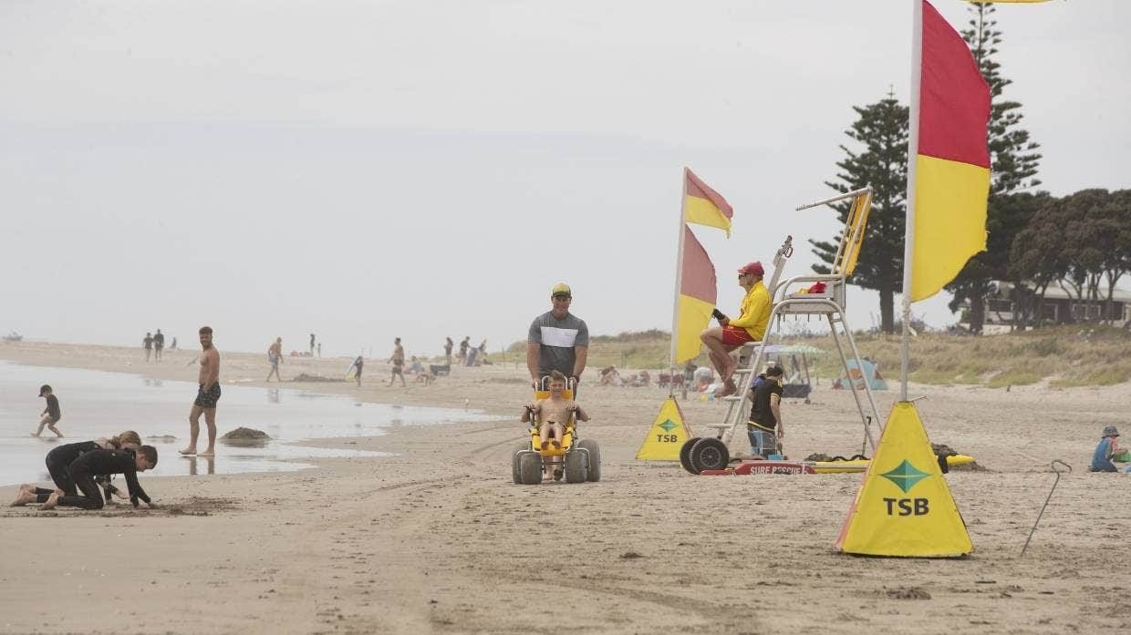 Zac Schultz being pushed down the sand in a beach wheelchair towards the sea at Whangamata