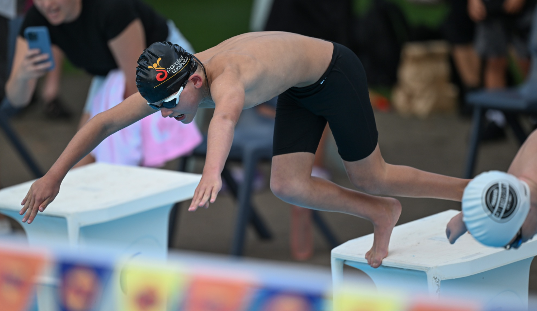Zac Schultz launching off the starting blocks in a Parafed Waikato cap at a para swimming meet in Hamilton